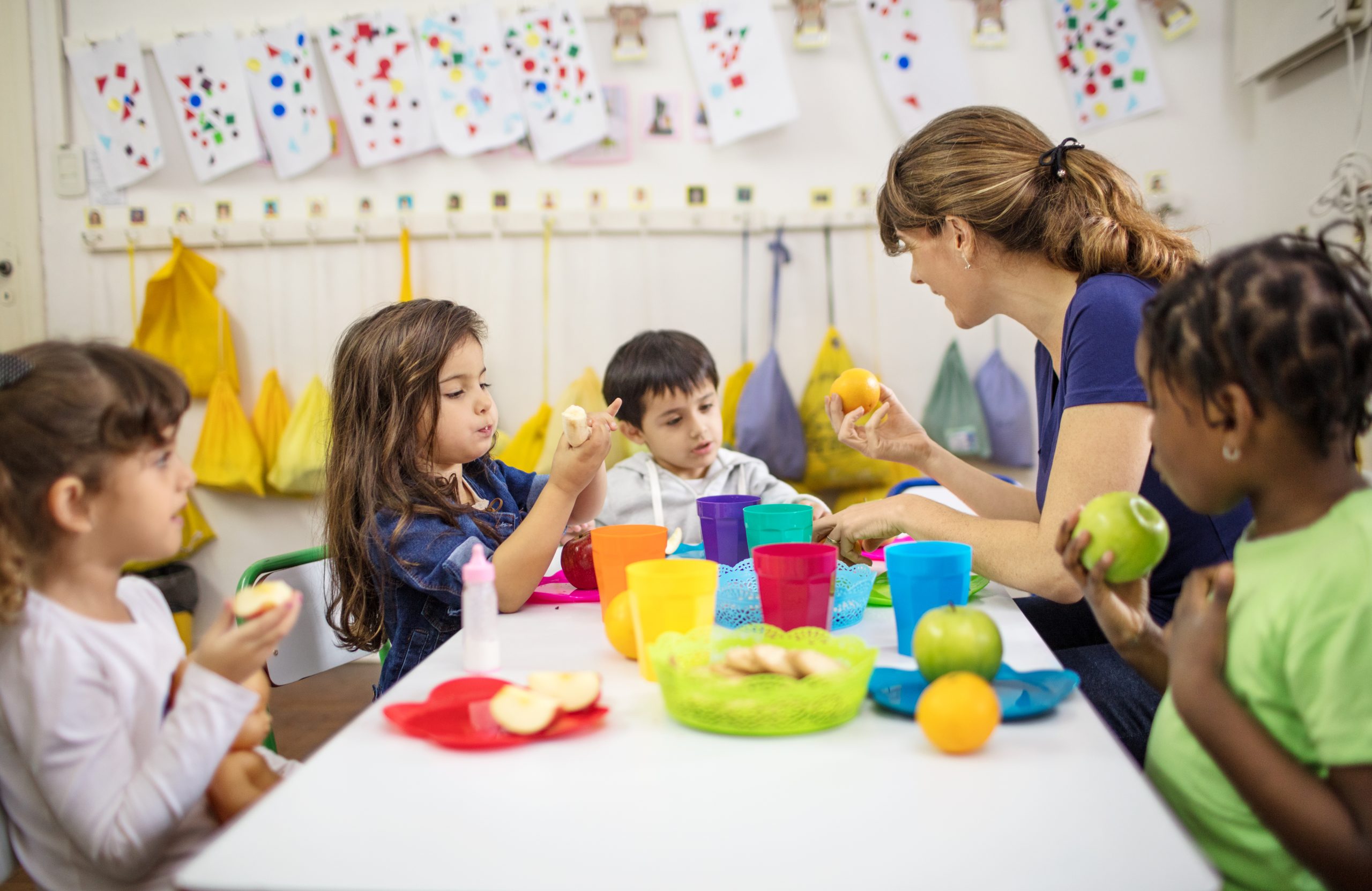 Children eating at a table with a nursery worker